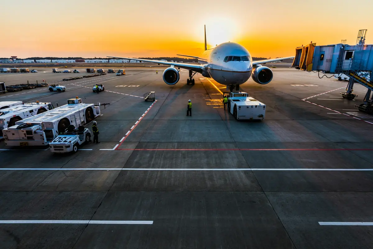 Wide-body aircraft on an airport apron at sunset with ground handling equipment
