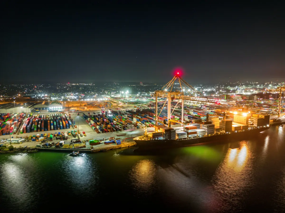 Aerial view of a container port at night with illuminated cranes and stacks