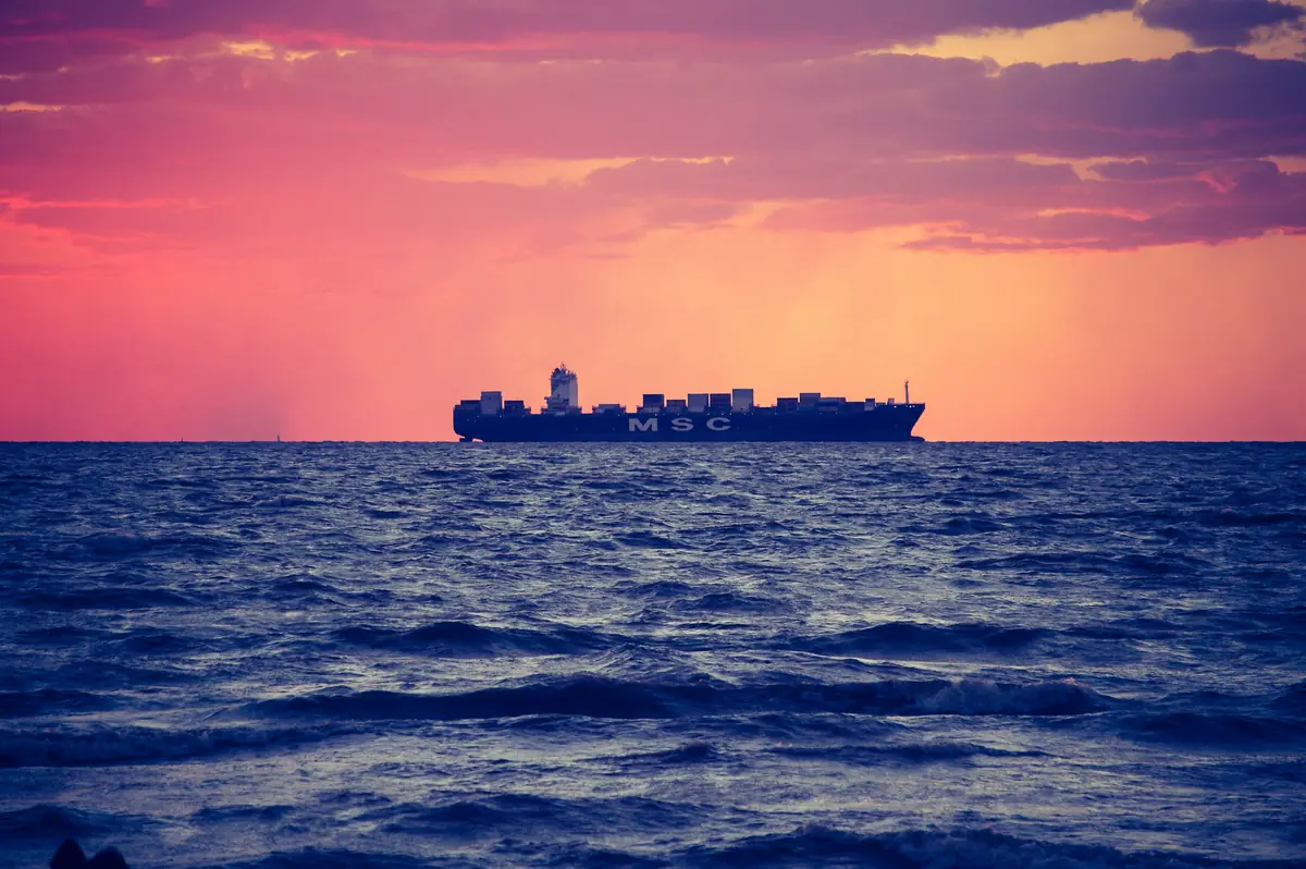 Container ship on the horizon under a pink and orange sunset sky